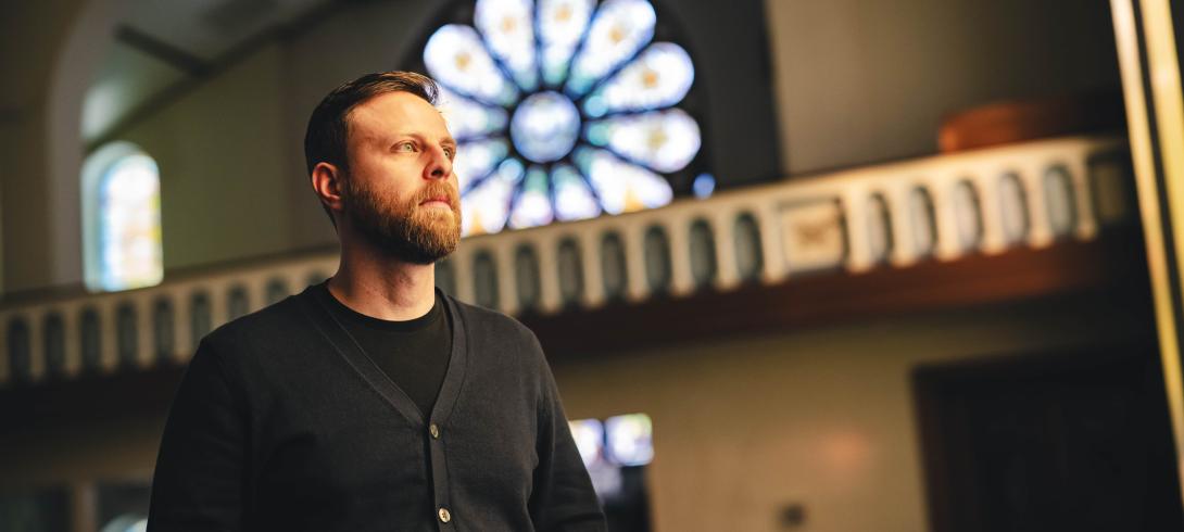Dean Caivano looks stoically off into the distance standing in a church converted into a church.